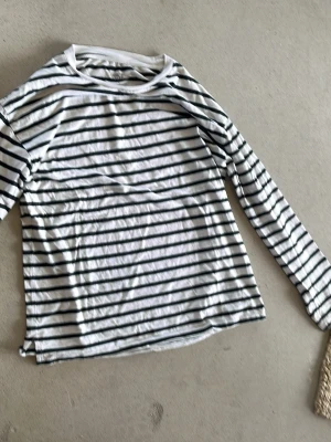 Randig långärmad topp från 157 - Säljer en vit långärmad topp från 157 med svarta horisontella ränder. Tillverkad i 100% bomull, perfekt för en avslappnad och stilren look. Klassisk rund halsringning och normal passform.