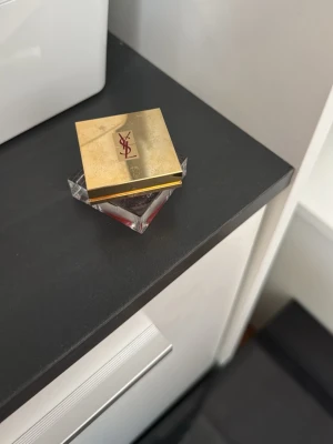 YSL rouge med guldfärgat lock - Lyxig  från Yves Saint Laurent i en snygg fyrkantig burk med guldfärgat lock och YSL-logga. Förpackningen är genomskinlig undertill och ger en exklusiv känsla. Perfekt för dig som vill ha en elegant touch till din sminkväska.