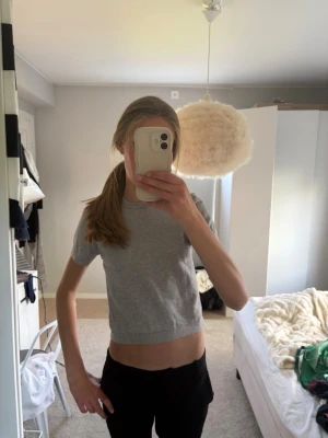 Grå croppad topp från Gina Tricot - En enkel och stilren grå croppad topp från Gina Tricot. T-shirten har korta ärmar och rund halsringning. 
