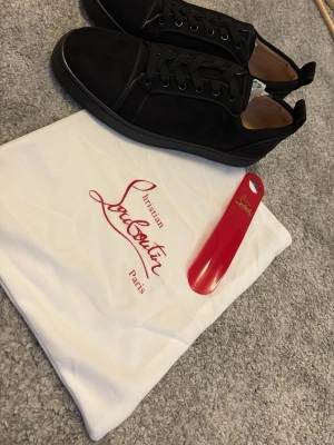 Svarta sneakers från Christian Louboutin - Stilrena svarta sneakers från Christian Louboutin i mocka och läderdetaljer. Klassisk låg modell med svarta snören och diskret logga. Kommer med originalpåse och röd skohorn med Louboutin-logga. Perfekta för dig som gillar exklusiva och trendiga skor.