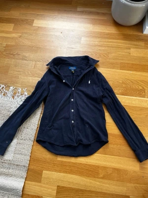 Mörkblå skjorta från Polo Ralph Lauren - Klassisk mörkblå skjorta från Polo Ralph Lauren. Skjortan har en liten broderad logga på bröstet och är tillverkad i bomull. Perfekt för en stilren och avslappnad look.