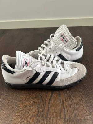 Adidas Samba vita sneakers - Klassiska Adidas Samba sneakers i vitt läder med grå mockadetaljer och svarta ränder på sidorna. Ena skon har lite färg på insidan och båda har lite slitna hälar på insidan men inget man tänker på, syns bara på nära håll. Nypris : ca 1500 SEK Pris : 300 SEK