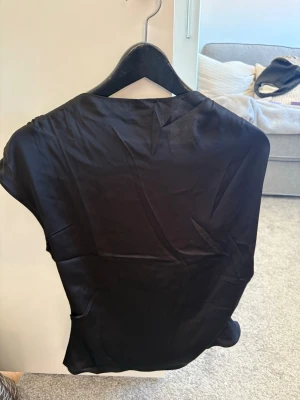 Svart topp - En stilren svart topp i slätt material med diskret dragkedja i ryggen. Toppen har en enkel, klassisk form och är perfekt för dig som gillar minimalistisk stil. Aldrig använd! 