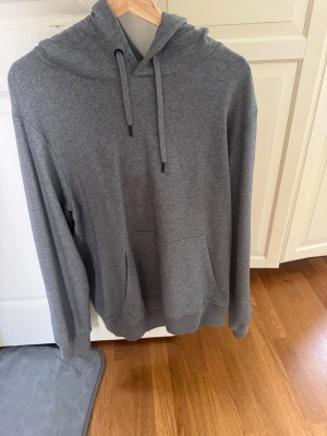 Grå hoodie från Canada Goose - Snygg grå hoodie från Canada Goose med klassisk känguruficka och huva med dragsko. Mjuk bomullsblandning och ikonisk Canada Goose-logga på ärmen. Perfekt för en chill och avslappnad stil.