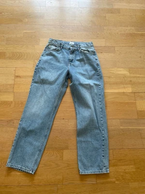 Blå raka jeans från grunt med klassisk passform - Säljer ett par ljusblå jeans med raka ben och klassisk femficksdesign. Jeansen har normal midja och är tillverkade i denim. Perfekta för dig som gillar en tidlös och avslappnad stil. Strlk 28 med justerbar midja