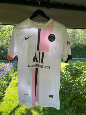 PSG Messi matchtröja vit/rosa Nike - Säljer en snygg PSG matchtröja från Nike i vitt med rosa och svart rand på framsidan. Tröjan har Messi 30 tryckt på ryggen och PSG-logga på bröstet. Tillverkad i lätt och ventilerande material, perfekt för fotboll eller träning.