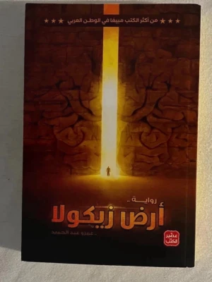 Ard Zykola av Amr Abdel Hamid - En arabisk skönlitterär roman med ett mystiskt omslag i bruna och orange toner. Boken är skriven av Amr Abdel Hamid och ges ut av förlaget عصير الكتب. Omslaget visar en person framför en gigantisk öppning i en stenmur, vilket ger en episk och äventyrlig känsla.