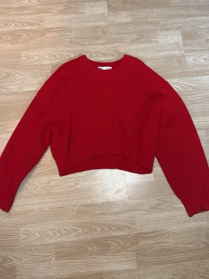 Röd stickad tröja från Zara - Röd stickad tröja från Zara med rund halsringning och ribbstickad struktur. Tröjan har en croppad passform och långa ärmar. I storlek L, tröjan har dock en lite fläk på ena ärmen.