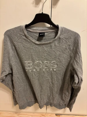 Grå sweatshirt från Hugo Boss - Snygg grå sweatshirt från Hugo Boss med broderad logga på bröstet. Tröjan har rund halsringning, långa ärmar och ribbade muddar. Perfekt för en avslappnad och stilren look.