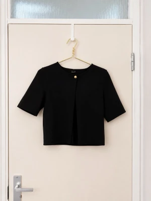 Kort svart kofta med guldknapp - Stilren svart kofta i kort modell med halvlånga ärmar och rund halsringning. Framtill stängs den med en dekorativ guldknapp. Perfekt att slänga över en topp för en clean look. Materialet känns mjukt och följsamt.