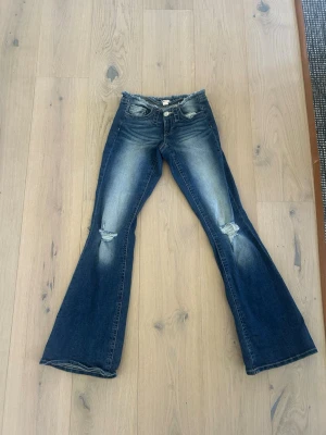 Blå bootcut jeans från Gina Tricot! - Säljer ett par blå bootcut jeans från Gina Tricot med fransig midja och slitningar på knäna. Jeansen har en klassisk femficksmodell och är tillverkade i denim med stretch. Perfekta för en trendig och avslappnad look. Storlek s! ALDRIG ANVÄNDA😍