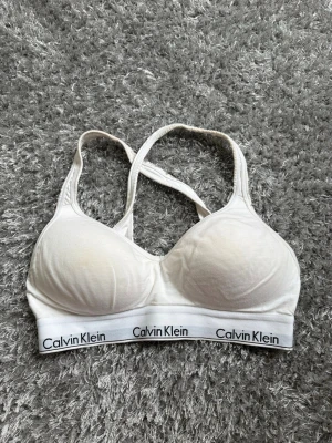 Vit Calvin Klein bh med korsade band - Snygg vit bh från Calvin Klein med vadderade kupor och korsade axelband. Pris kan alltid diskuteras!