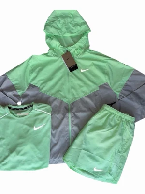 Nike mintgrön träningsset - Snyggt träningsset från Nike i mintgrönt och ljusgrått. Setet består av en tunn jacka med huva och dragkedja, matchande shorts samt en t-shirt. Alla delar har Nike-logga framtill. Perfekt för träning eller chill. Materialet känns lätt och andas bra.