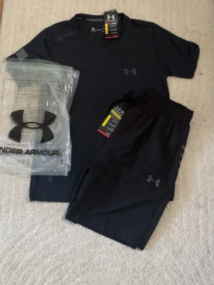 Svart träningsset från Under Armour - Snyggt svart träningsset från Under Armour med t-shirt i storlek M och shortsen i storlek L för en skönare passform 