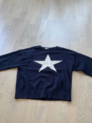 Svart stickad tröja med stjärna - Cool svart stickad tröja från Gina Tricot med en stor vit stjärna på bröstet. Tröjan har rund halsringning och långa ärmar. Perfekt för dig som gillar enkel men snygg design.