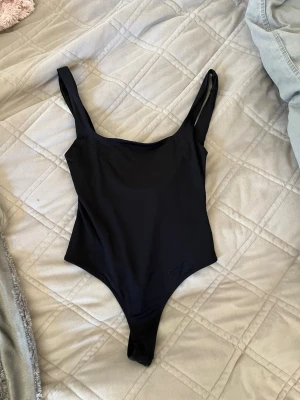 Zara body - En stilren svart body med breda axelband och rundad urringning både fram och bak. Modellen är enkel och tight, perfekt att styla till olika outfits. Materialet känns stretchigt och mjukt mot huden. Populära bodyn från Zara, aldrig använd! 