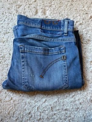 Blå jeans med broderad ficka - Snygga blå jeans från dondup i modell George med klassisk femficksdesign och en unik broderad detalj på bakfickan. Jeansen har en rak passform och är tillverkade i mjukt denimtyg. Perfekta för en avslappnad och trendig look.