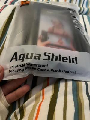 Aqua Shield vattentätt mobilskal - Universal vattentätt mobilskal med flytande air bag och stor kapacitet. Skalet har säker låsning och är reptåligt, perfekt för att skydda mobilen vid vattenaktiviteter. Materialet är plast och färgen är svart.