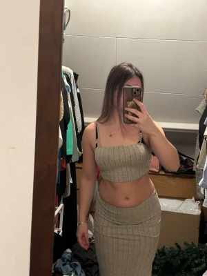 Beige ribbat set med kjol och topp - Säljer ett snyggt beige ribbat set med en croppad topp med smala axelband och en matchande hög kjol med slits bak. Setet är figurnära och stretchigt, perfekt för dig som gillar trendiga och bekväma plagg. Passar S och XS