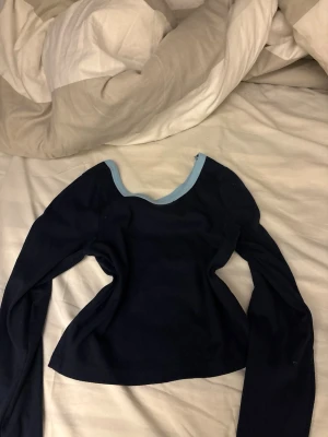 Mörkblå långärmad topp med ljusblå kant - Snygg mörkblå långärmad topp med ljusblå kant runt den vida, rundade halsringningen. Modellen är croppad och har en slim passform som framhäver figuren. Perfekt att styla med höga jeans eller kjol för en trendig look.