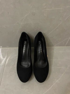 Svarta pumps med klack - Stilrena svarta pumps med rund tå och bred klack. Skorna har en klassisk siluett och är tillverkade i ett material som ser ut som mocka. 