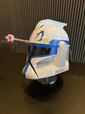 Star Wars Clone Trooper hjälm - Cool Clone Trooper hjälm från Star Wars med vit och blå design, svart visir och detaljer i gult. Hjälmen har en rörlig antenn med röd LED-lampa och är tillverkad i plast. Perfekt för cosplay eller maskerad för dig som gillar sci-fi och galaktiska äventyr. Alla funktioner fungerar som de ska. 