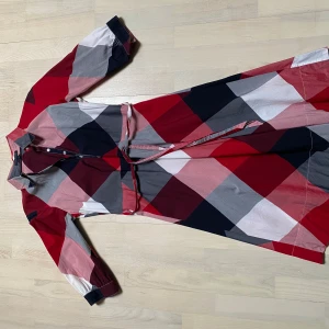Rutig klänning Tommy Hilfiger - Snygg midi klänning i rött, blått och vitt med ett rutigt mönster. Klänningen har tre kvarts långa ärmar och rem i midjan för en fin passform. Perfekt för en klassisk och stilren look. Tommy Hilfiger strl 4. 