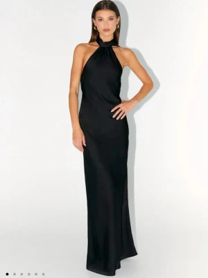 Svart långklänning/balklänning med halterneck - Elegant svart långklänning med halterneck och öppen rygg. Klänningen har en snygg knytning i nacken och baktill, vilket ger en stilren och modern look. Materialet har en lätt glans och faller fint längs kroppen.             Fick hem förra veckan, från ”Peppermayo” men var lite för stor för mig så säljer därför här.