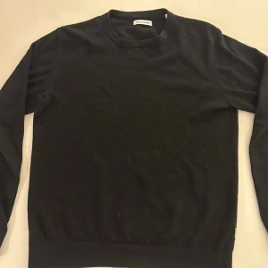 Svart stickad tröja - En enkel och stilren svart. Tröjan har rund halsringning, långa ärmar och ribbade muddar vid ärmslut och nederkant. Perfekt basplagg för alla tillfällen och lätt att matcha med andra plagg.