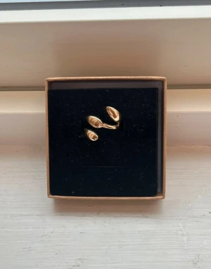 Guldfärgad ring med droppformad design - Snygg guldfärgad ring med tre droppformade detaljer i modern och stilren design. Ringen har en öppen form som ger en unik look och passar perfekt för dig som gillar trendiga accessoarer. Materialet ser ut att vara metall med blank finish.