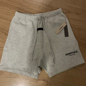 Grå shorts från Essentials Fear of God - Snygga ljusgrå shorts från Essentials Fear of God med elastisk midja och snörning. Mjukt material och diskret logga framtill. Perfekta för en avslappnad stil.