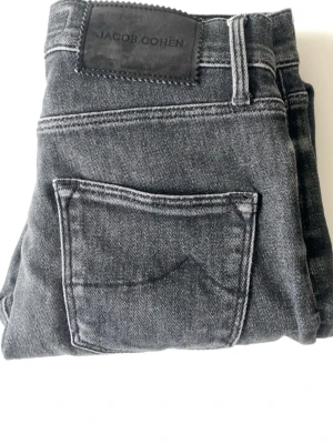 Svarta jeans från Jacob Cohen - Snygga svarta jeans från Jacob Cohen med klassisk femficksmodell och raka ben. Jeansen är tillverkade i mjukt denimtyg och har en diskret logopatch bak i midjan. Perfekta för en stilren och avslappnad look.