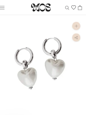 WOS örhängen med pärlhjärtan - Säljer ett par snygga örhängen från WOS med silverfärgade hoops och vita hjärtformade pärlor som hänger ned. Perfekta för att ge din look en söt och trendig touch. Materialet är metall och pärlliknande detaljer. Dom är helt nya och oöppnade från paketet!