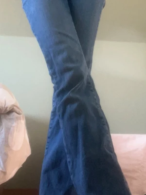 Blå bootcut jeans med utsvängda ben - Säljer ett par klassiska blå bootcut jeans med utsvängda ben. Jeansen har hög midja och är tillverkade i ett stretchigt denimtyg som sitter snyggt över höfterna och låren. Perfekta för dig som gillar retrostil och vill ha ett par jeans som sticker ut.