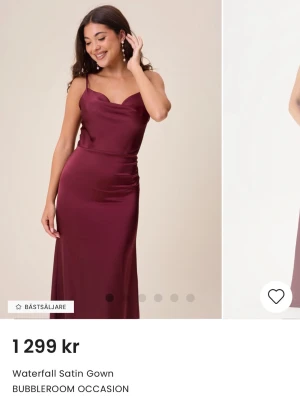 Vinröd långklänning i satin från Bubbleroom - Snygg vinröd långklänning från Bubbleroom i satin med vattenfallsringning och smala axelband. Klänningen har en elegant passform och är perfekt för speciella tillfällen. Materialet är glansigt och följsamt, vilket ger en lyxig känsla Endast använd en gång.