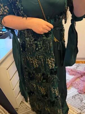 Mörkgrön kurdisk långklänning med paljetter - Unik mörkgrön långklänning med broderade detaljer och stora paljetter. Klänningen har knytband i midjan och vid ärmarna 