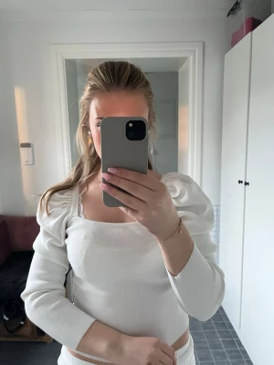 Vit topp med puffärmar - Säljer en vit topp med puffade axlar och trekvartsärm. Toppens material är ribbad och den har en fyrkantig halsringning som ger en trendig look. Perfekt för dig som gillar stilrena och moderna plagg.