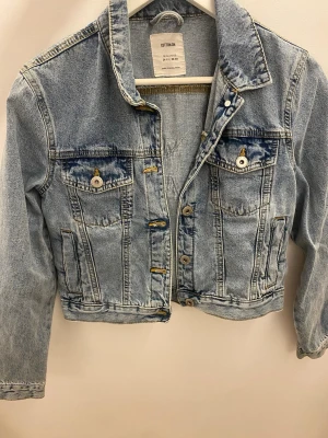 Ljusblå jeansjacka med fjärilsdetalj - Snygg ljusblå jeansjacka från Cotton On med cool fjärilsapplikation på ryggen. Jackan har två bröstfickor med knappar, klassisk krage och croppad passform. 