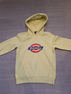 Gul hoodie från Dickies med logga storlek XS - Snygg gul hoodie från Dickies med stor färgglad logga på bröstet. Klassisk känguruficka framtill och huva med dragsko. Tillverkad i mjukt bomullsmaterial som är skönt att ha på sig. Anmärkningar på plagget ses på bilder 
