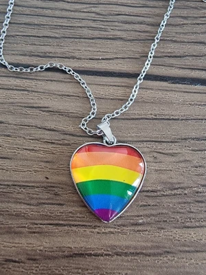Halsband med regnbågshjärta - Snyggt halsband med ett hjärtformat hänge i regnbågens färger. Hänget har en blank glasyta och sitter på en tunn silverfärgad kedja. Kedjans längd 45 + 5 cm. Berlock 2×2 cm. Perfekt accessoar för att visa din pride och sprida färg i vardagen.