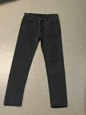 Mörkgrå jeans från Wrangler - Snygga mörkgrå jeans från Wrangler med klassisk femficksdesign och raka ben. Jeansen har detaljer i kopparfärgad metall och bälteshällor. Perfekta för dig som gillar en stilren och enkel look.hlet ny