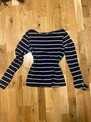 Marinblå randig långärmad topp - Snygg marinblå topp med vita horisontella ränder och långa ärmar. Figurnära passform som markerar midjan och rundad halsringning. Perfekt för en trendig och avslappnad look. 