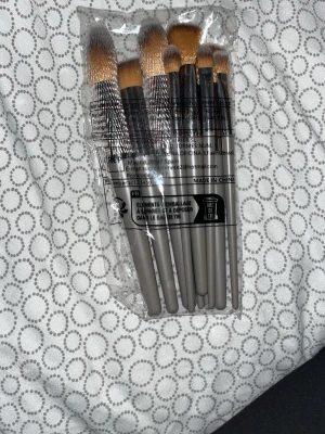 Set med sminkborstar i grått - Säljer ett set med sju sminkborstar med gråa handtag och täta, mjuka borst i beige och brunt. Perfekt för både ögonskugga och ansiktsmakeup. Borstarna har stilren design och kommer i en praktisk plastförpackning.