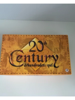 20th Century århundradets spel - Sällskapsspel med guldfärgad låda och detaljer, inkluderar spelplan, spelpjäser, kort och spelregler. Perfekt för spelkvällar med vänner eller familj. Allt material har matchande design med 1900-tals tema. Lite kantstött på kartongens ena sida, annars mycket gott skick. Nypris 599:-