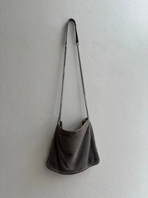 Grå Stella McCartney väska  - Snygg grå handväska från Stella McCartney.  Väskan har kedjerem och dekorativa kedjedetaljer runt kanterna.