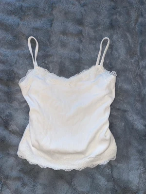 Vit ribbad linnetopp med spets - Söt vit linnetopp med tunna axelband och ribbad struktur. 