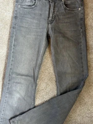 Grå jeans med vida ben - Snygga grå jeans med vida ben och klassisk femficksdesign. Jeansen har en lätt tvättad look och råa kanter nertill för en avslappnad vibe. Perfekta att matcha med sneakers eller boots. Materialet känns mjukt och följsamt, troligtvis bomull med lite stretch. Skriv om ni vill ha bild med jeansen på.