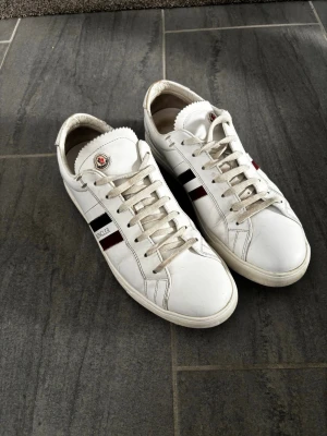 Vita Moncler sneakers med ränder - Nypris runt 4-5 tusen vi säljer dom för ett schysst pris, kan även gå ner i pris vid bra affär🤩💯 Snygga vita sneakers från Moncler med klassiska röda och marinblå ränder på sidan samt Moncler-logga på plösen. Skorna är 43-44 tycker dom är lite för stora för mig därav säljer jag. Äkta moncler.