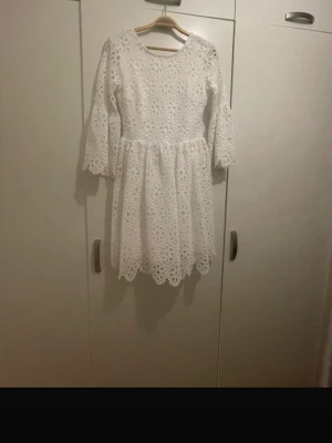 Vit spetsklänning med trumpetärm - Superfin vit kortklänning med blommig spets och trumpetärmar. Klänningen har rund halsringning och är helfodrad, vilket gör den både bekväm och snygg. Perfekt för sommarens alla tillfällen!