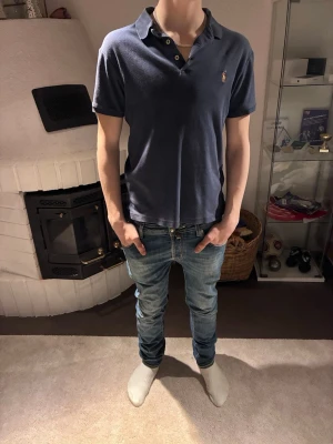 Blå pikéskjorta från Polo Ralph Lauren - Säljer en blå pikétröja från Ralph Lauren med klassisk krage och korta ärmar. Tröjan har en liten broderad logga på bröstet och är tillverkad i mjuk bomull. Perfekt för en stilren och avslappnad look. Tröjan är givetvis äkta. Tröjan är även i mycket gott skick: 9/10.